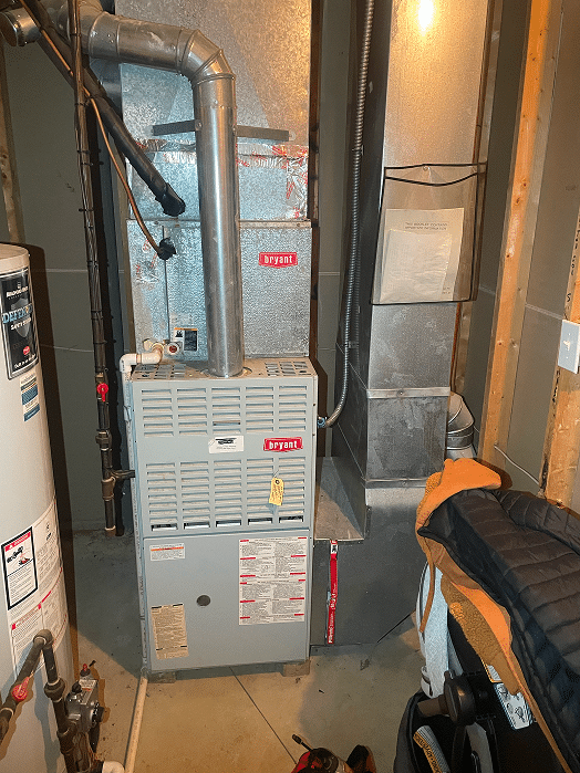 A gray Bryant gas furnace installed in a residential basement in Hilliard, Ohio, featuring a yellow service tag and positioned next to a water heater.